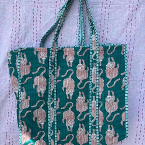 May include: A teal blue tote bag with white and pink tiger print. The bag has two long straps and a wide base.