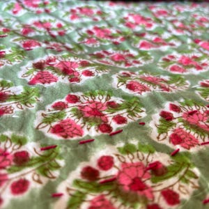 May include: Close-up of a green fabric with a pink floral pattern. The fabric is quilted with small stitches.