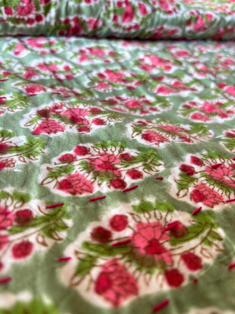May include: Close-up of a green fabric with a pink floral pattern. The fabric is quilted with small stitches.
