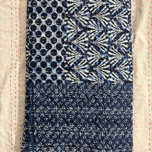 Op de afbeelding: Een blauwe en witte kantha-deken met een patchwork-ontwerp. De deken heeft drie verschillende patronen: stippen, spiralen en een geometrisch ontwerp.
