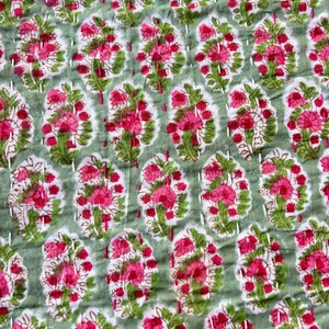 May include: A green and pink floral patterned fabric with white stitching. The fabric has a repeating pattern of pink flowers with green leaves.