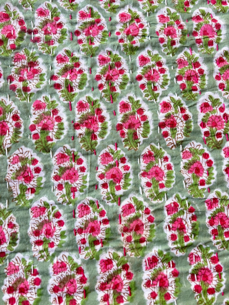 May include: A green and pink floral patterned fabric with white stitching. The fabric has a repeating pattern of pink flowers with green leaves.