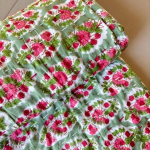 May include: A green and pink floral kantha quilt with a repeating pattern of flowers and leaves. The quilt is made of cotton and is hand-stitched.