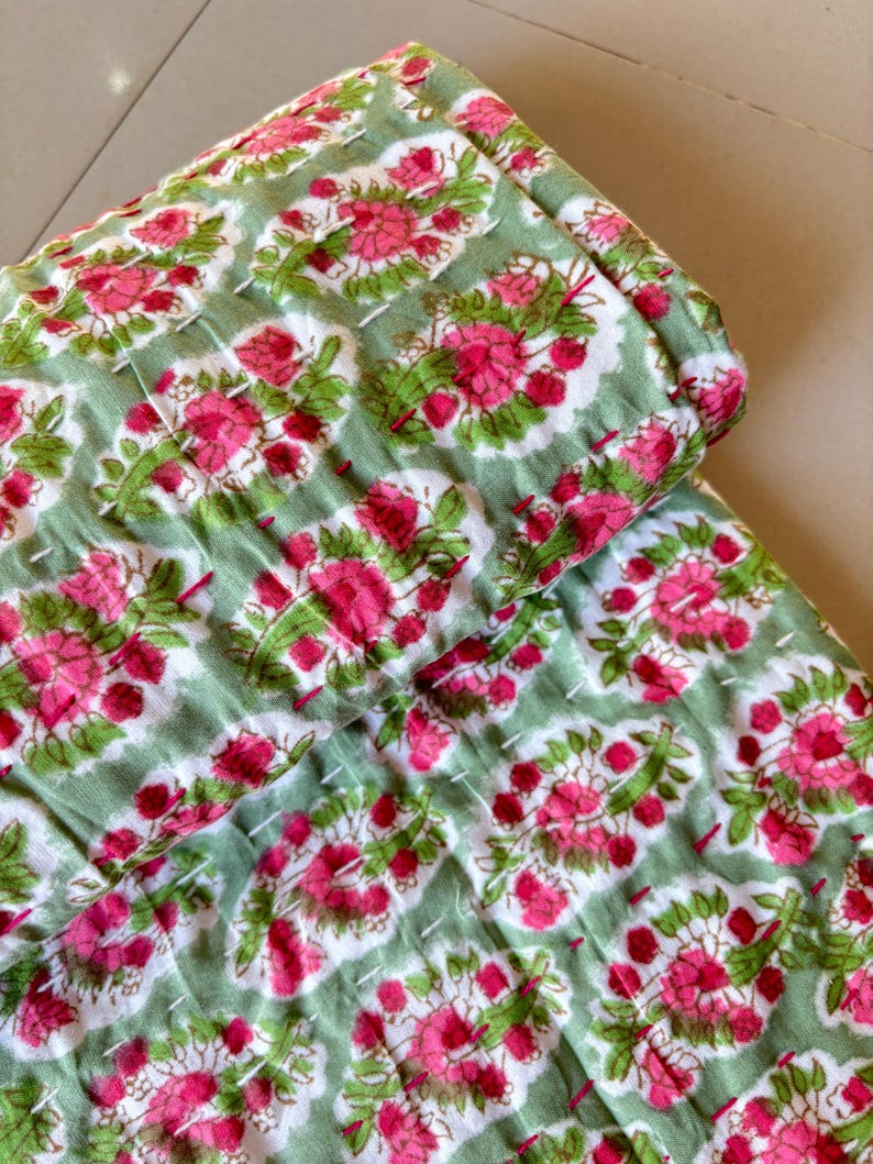 May include: A green and pink floral kantha quilt with a repeating pattern of flowers and leaves. The quilt is made of cotton and is hand-stitched.