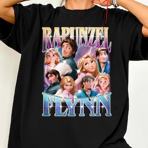 Puede incluir: Camiseta negra con un diseño gráfico de personajes de la película animada "Enredados", con los nombres "Rapunzel" y "Flynn" en una fuente estilizada. El diseño incluye múltiples retratos de personajes en colores vibrantes.