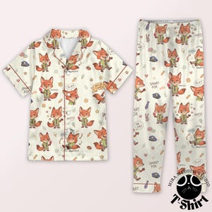 May include: Cream-colored pajama set with a repeating pattern of cartoon foxes in various poses, along with text like "Smart Fox" and "Wild Times." The set includes a button-down shirt and matching pants.