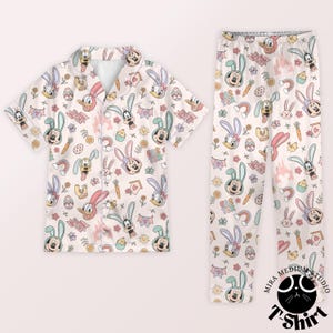 May include: A two-piece pajama set featuring a light beige background with an all-over print of cartoon characters, Easter eggs, carrots, and rainbows. The short-sleeved top and pants are decorated with Mickey Mouse, Donald Duck, and other Disney characters.