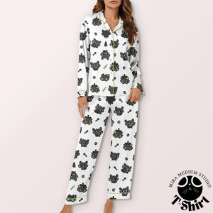 Puede incluir: Conjunto de pijama blanco con un estampado repetido de caras de gatos negros de dibujos animados, llaves y huesos. La parte superior de manga larga y los pantalones tienen ribetes verdes. El conjunto de pijama est&aacute; hecho de un material suave y c&oacute;modo.