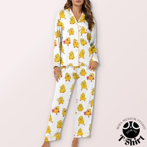 May include: White pajama set with a repeating pattern of yellow cartoon chicks. The long-sleeved top and pants are trimmed with yellow piping. The pajama set is made of a soft, comfortable material.
