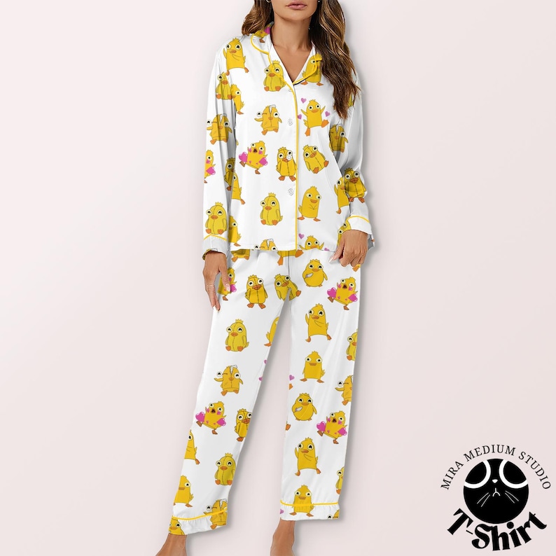 May include: White pajama set with a repeating pattern of yellow cartoon chicks. The long-sleeved top and pants are trimmed with yellow piping. The pajama set is made of a soft, comfortable material.