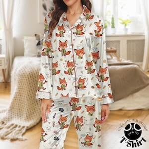 May include: White pajama set with a repeating pattern of cartoon foxes in various poses, with text bubbles saying "Sly!", "Cool", and "Hustle". The pajamas have brown trim and buttons.