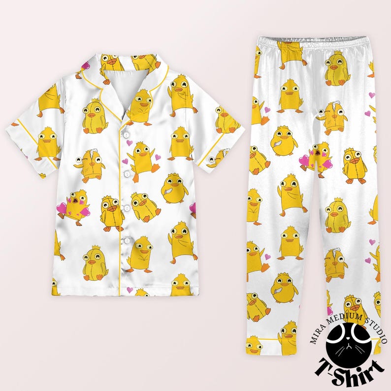 May include: White pajama set with a repeating pattern of yellow cartoon ducks and pink hearts. The short-sleeved top has yellow trim and buttons. The matching pants complete the set, perfect for a comfortable night's sleep.