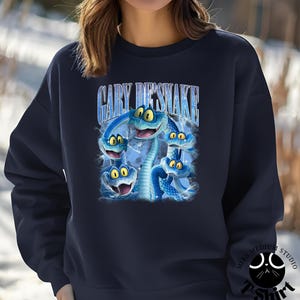 Peut inclure: Sweat-shirt bleu marine avec un motif de cinq serpents bleus de dessin anim&eacute; aux yeux jaunes. Le texte "GARY DESNAKE" est arqu&eacute; au-dessus des serpents. Le sweat-shirt a un col rond et des manches longues.