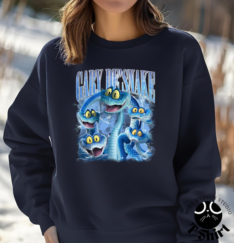 Peut inclure: Sweat-shirt bleu marine avec un motif de cinq serpents bleus de dessin anim&eacute; aux yeux jaunes. Le texte "GARY DESNAKE" est arqu&eacute; au-dessus des serpents. Le sweat-shirt a un col rond et des manches longues.