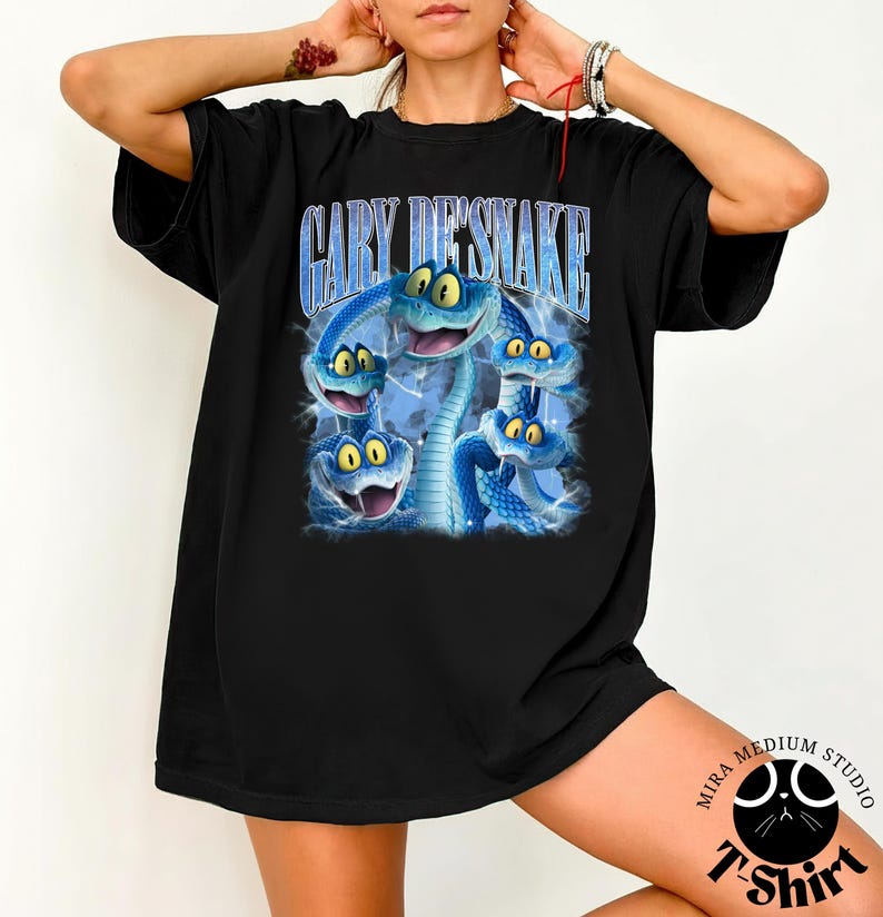 Peut inclure: T-shirt noir avec un motif de serpents bleus de dessin anim&eacute; aux yeux jaunes. Le texte "GARY DESNAKE" est imprim&eacute; au-dessus des serpents dans une police bleue stylis&eacute;e. Le t-shirt a une coupe ample.