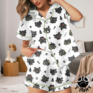 Puede incluir: Conjunto de pijama blanco con un estampado repetido de dragones de dibujos animados negros, calaveras y espinas de pescado. La parte superior de manga corta y los pantalones cortos est&aacute;n ribeteados con ribetes verdes. El conjunto de pijama es de un material suave y sedoso.