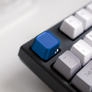 Op de afbeelding: Een blauwe toetsenbord-toetsdop met een vierkante vorm en een licht afgeronde bovenkant. De toetsdop is gemaakt van glad, hard plastic en heeft een matte afwerking.