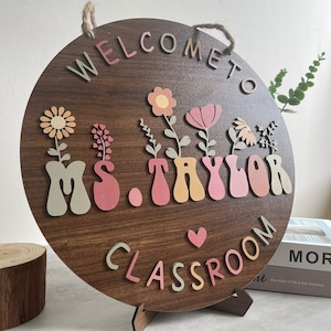 May include: Welcome to Ms. Taylor's Classroom sign with a brown wooden background and colorful letters. The sign has a heart and flowers.
