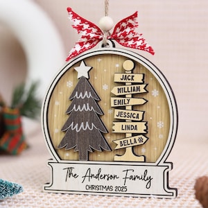 May include: Wooden Christmas ornament with a tree and directional signs with names. The ornament has a red and white bow and the text "The Anderson Family CHRISTMAS 2025".