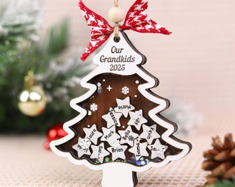 May include: A wooden Christmas tree ornament with the text "Our Grandkids 2025". The ornament has a white outline and a brown center with star-shaped name tags. It is decorated with a red and white bow.