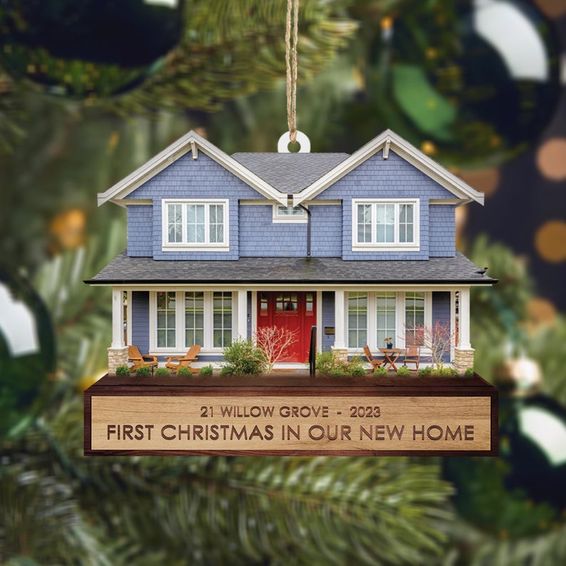 May include: A blue and white house ornament with a red door and a wooden plaque that reads "21 Willow Grove - 2023 First Christmas in Our New Home".