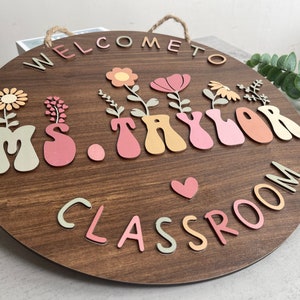 May include: A round wooden sign with the text "Welcome to Ms. Taylor's Classroom" in colorful letters. The letters are decorated with flowers and hearts.
