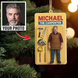 May include: A personalized Christmas ornament featuring a man in a carpenter's apron, with the text "MICHAEL THE CARPENTER." The ornament includes a photo area labeled "YOUR PHOTO" and illustrations of tools like a hammer, saw, and circular saw.