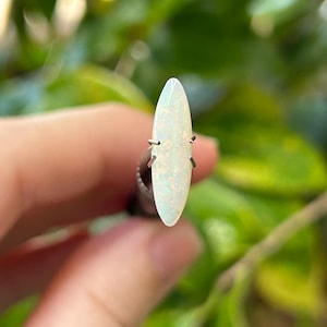 May include: A white oval opal gemstone with a slight iridescent sheen, set in a silver prong setting.