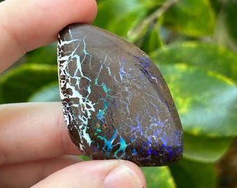 Puede incluir: Un ópalo marrón, blanco y azul con un patrón natural único. El ópalo es una piedra en bruto sin cortar con una superficie lisa y pulida.