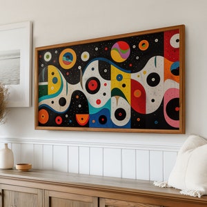 May include: A framed abstract painting with a black background and colourful geometric shapes, including circles, squares, and wavy lines. The painting is in a wooden frame and is hanging on a white wall.