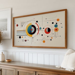 Op de afbeelding: Een ingelijste abstracte kunstprint met een geometrisch ontwerp met cirkels, lijnen en vierkanten in tinten rood, geel, blauw, zwart en wit.
