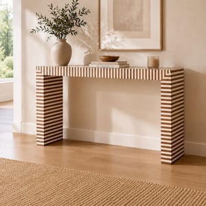 May include: A rectangular console table featuring a repeating horizontal striped pattern in alternating white and brown tones. The table has a flat top surface and two vertical side supports, creating a clean, geometric silhouette.