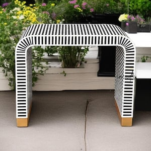 May include: A contemporary, U-shaped side table featuring a black and white striped design. The table has a white frame with black stripes and gold-coloured feet. The table is approximately 61 cm long, 30 cm wide, and 46 cm high.