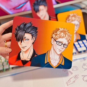 Puede incluir: Impresi&oacute;n art&iacute;stica rectangular con dos personajes masculinos de estilo anime sobre un fondo degradado de rojo a naranja. Uno tiene cabello negro y una parte superior roja. El otro tiene cabello rubio, gafas y una parte superior azul.