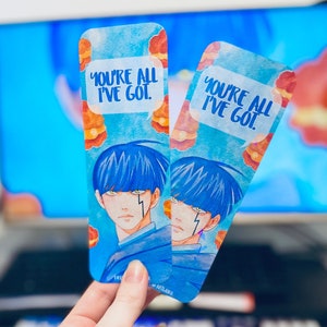 May include: Two blue and white watercolour bookmarks with a stylised illustration of a person with blue hair and a lightning bolt on their face. The text on the bookmarks reads "You're all I've got."