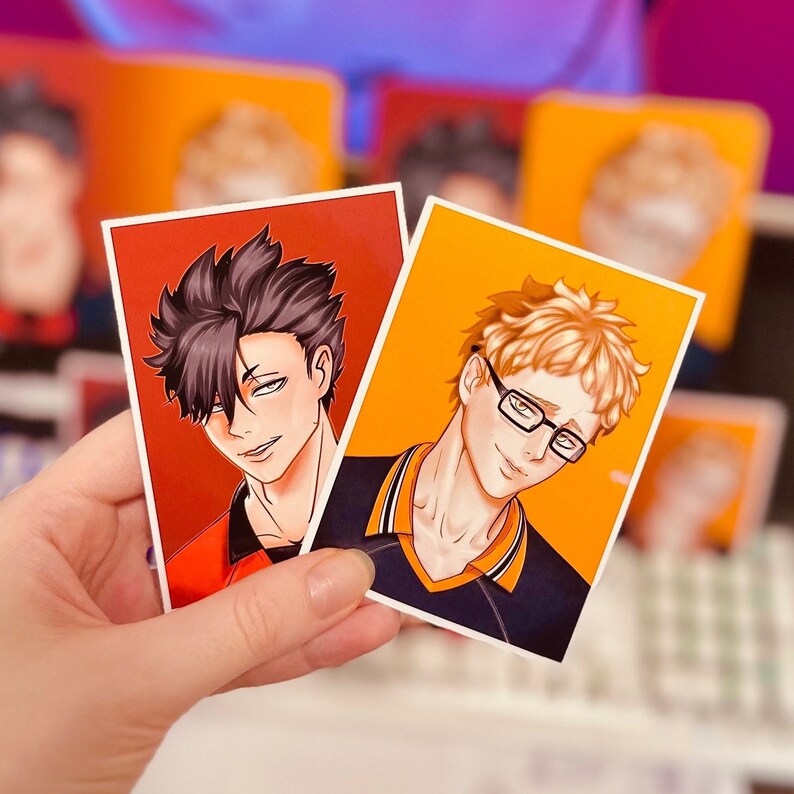 Puede incluir: Dos pegatinas rectangulares con ilustraciones de estilo anime de personajes masculinos. Una pegatina tiene un fondo rojo y un personaje con cabello oscuro. La otra tiene un fondo naranja y un personaje con cabello rubio y gafas.