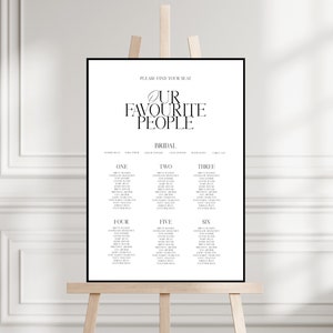 May include: Black and white wedding seating chart with the text "Please find your seat" and "Our Favourite People" with a leaf design. The chart lists table numbers one through six with guest names.