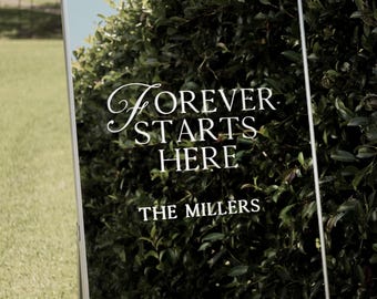May include: A white mirror with the text "Forever Starts Here. The Millers" on a black background. The mirror is surrounded by green foliage.