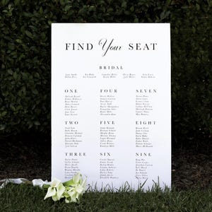 May include: A white wedding seating chart with the text "Find Your Seat" and "Bridal" at the top. The chart lists guest names by table number, from one to nine.