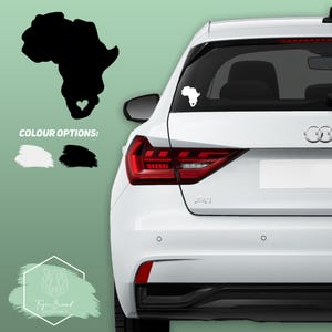 May include: A white car with a black outline of the continent of Africa with a heart in the middle on the back window. The car is parked on a green background. The image also shows a black and white outline of the continent of Africa with a heart in the middle.