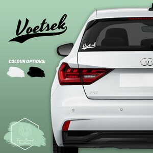 May include: A white car with a black and white vinyl decal on the back window that says "Voetsek". The decal is in a retro font style. The car is parked on a green background. The image also includes a logo for Tiger Brand.