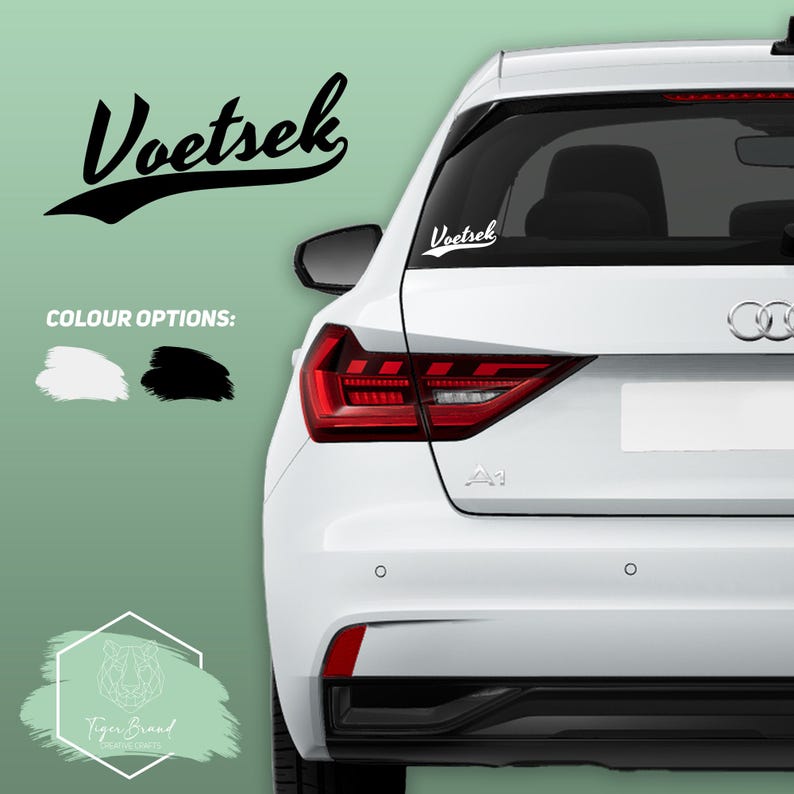May include: A white car with a black and white vinyl decal on the back window that says "Voetsek". The decal is in a retro font style. The car is parked on a green background. The image also includes a logo for Tiger Brand.