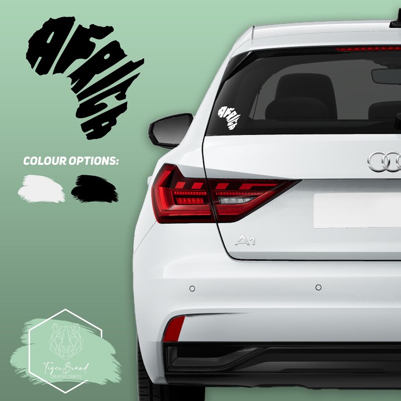 May include: A white car with a black "Africa" decal on the back window. The decal is shaped like the continent of Africa and the word "Africa" is spelled out within the outline of the continent. The car is parked on a green background.