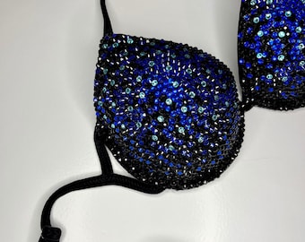 May include: A black bikini top and bottom with blue and teal rhinestones. The top has a halter style strap and the bottom is a simple, low-rise style.