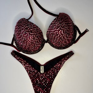 Puede incluir: Bikini de terciopelo burdeos con adornos de cristal. La parte superior tiene un estilo halter y la parte inferior es un corte atrevido. La marca "performance" está impresa en la parte inferior.