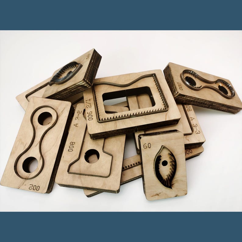 May include: A collection of light-coloured wooden die-cutting blocks featuring various metal blade shapes embedded in the surface. Each block is marked with numerical identifiers such as 002, 800, 60, and 200, used for precision cutting of materials.