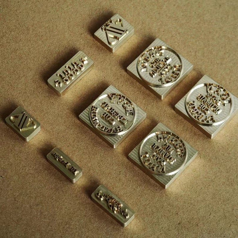 May include: Nine brass stamps with different designs and text. The stamps are square and rectangular in shape and have a gold finish.