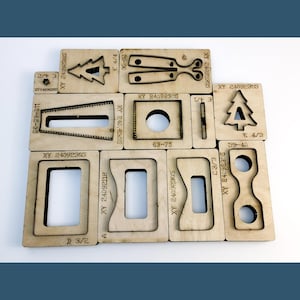 May include: A collection of light-coloured wooden die-cutting plates featuring various geometric and decorative shapes, including trees, rectangles, and circles. Each plate is engraved with alphanumeric codes such as XY 24092305, E 4/4, and 20-90, indicating specific model identifiers for crafting.