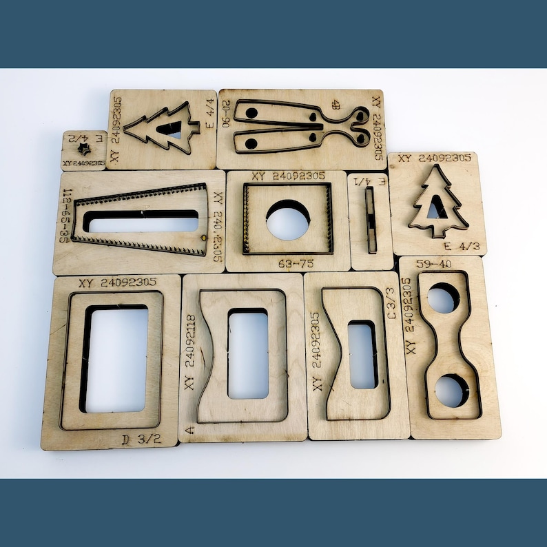 May include: A collection of light-coloured wooden die-cutting plates featuring various geometric and decorative shapes, including trees, rectangles, and circles. Each plate is engraved with alphanumeric codes such as XY 24092305, E 4/4, and 20-90, indicating specific model identifiers for crafting.