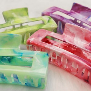 Puede incluir: Cuatro pinzas para el pelo de colores con un diseño de mármol. Las pinzas son en tonos de verde, morado, rosa y blanco.